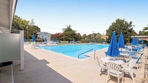 Une piscine entourée d’arbres et de bâtiments, avec des chaises longues et des parasols.