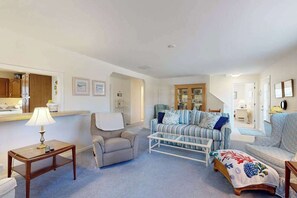 A living room with a sofa, armchairs, a coffee table, a lamp, and a kitchen area with cabinets. - Bethany West Retreat W/ Shared Pool & Ideal Location Close to Trolley stop (Bethany Beach)