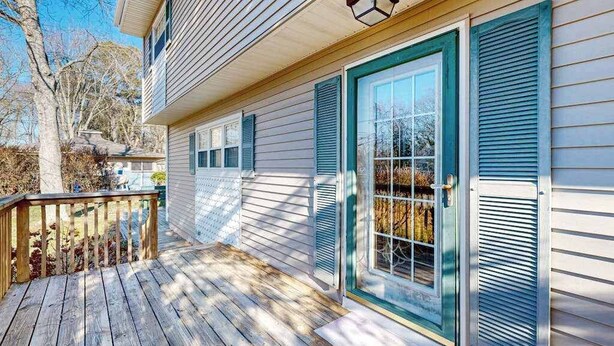 Une maison avec une terrasse en bois, une porte d’entrée dotée de panneaux de verre et une fenêtre avec des volets.