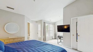 Un dormitorio con cama, televisor, espejo y puerta que da a otra habitación.