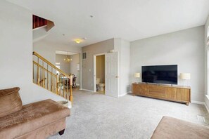 A living room with a staircase, a TV, and a wooden cabinet. - South Hampton townhome with shared pool & tennis courts (Ocean View)