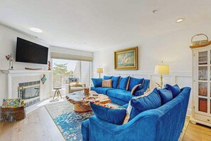 Un salon avec un canapé bleu, un téléviseur à écran plat, une cheminée et une grande fenêtre.