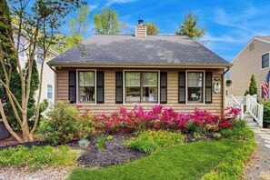 A two-story house with a front porch, a chimney, and a well-maintained garden with colorful flowers. - Charming Beach home with central ac, spacious Living Room and private deck (Bethany Beach)