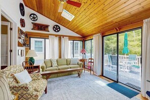 A cozy living room with a wooden ceiling, a sofa, a bench, and a view of the outdoors through large windows. - Charming Beach home with central ac, spacious Living Room and private deck (Bethany Beach)