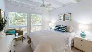 A bedroom with a bed, two bedside tables, a ceiling fan, and a window with a view of trees. - Ocean Village Beach block, pet friendly house w/patio, balcony, gas grill & WIFI (Bethany Beach)