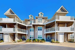 A multi-story building with balconies, a central entrance, and a clear sky. - Bethany Bay spacious condo w/shared pool, water view & golf course (Ocean View)