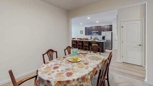 A dining area with a table covered in a floral tablecloth, surrounded by wooden chairs.
