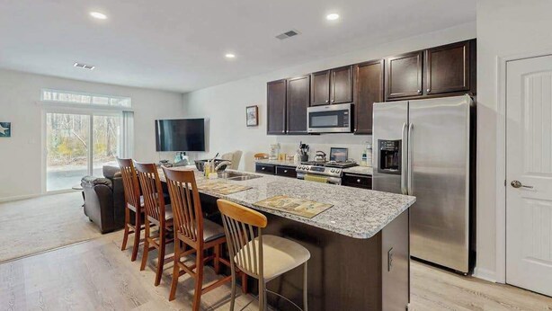 A modern kitchen with dark cabinets, stainless steel appliances, and a large island with bar stools.