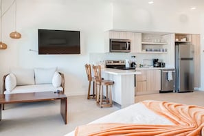 Une cuisine moderne dotée d’un îlot central, d’un coin repas avec un canapé et des chaises, et d’un téléviseur fixé au mur.
