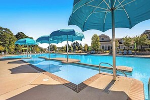 A swimming pool with lounge chairs and umbrellas, surrounded by buildings. - Ocean View Beach Club house with shared pool, sports courts, & gym (Ocean View)
