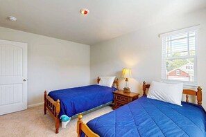 Ein Schlafzimmer mit zwei Betten, einem Nachttisch mit Lampe, einer weißen Tür und einem Fenster mit Jalousien.