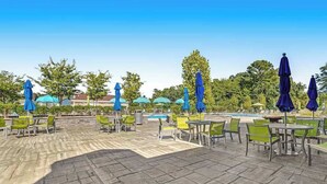 Une terrasse extérieure avec un sol en pierre, des chaises vertes et jaunes, et des parasols bleus.