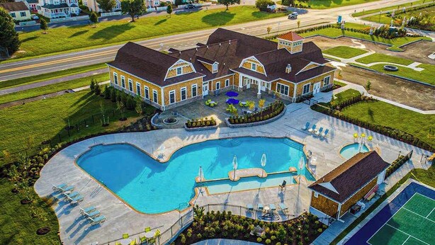 Une grande piscine avec des chaises longues, un court de tennis et une maison avec une allée.