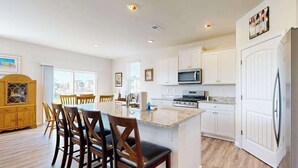 Une cuisine moderne avec des meubles blancs, un îlot central et un coin repas doté de chaises en bois.