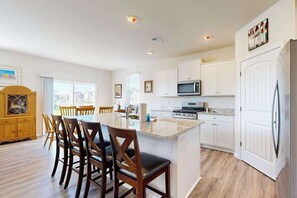 A modern kitchen with white cabinets, a central island, and a dining area with wooden chairs. - Ocean View Beach Club house with shared pool, sports courts, & gym (Ocean View)