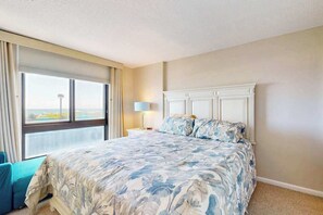 A hotel room with a large bed, a nightstand, a lamp, and a view of the city. - Sea Colony Ocean 1st floor condo w/ elevator, tennis court, and basketball court (Bethany Beach)