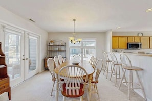 A dining area with a wooden table and white chairs, a kitchen with wooden cabinets, and a chandelier. - Sea Colony Tennis townhome w/community pools, tennis/pickleball, gym (Bethany Beach)