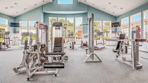 Ein Fitnessstudio mit verschiedenen Trainingsgeräten, großen Fenstern und hoher Decke.