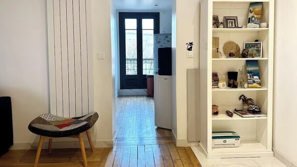 Een hal met een houten vloer, een witte radiator, een stoel en een witte wandplank met diverse spullen.
