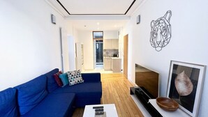 Een moderne woonkamer met een blauwe bank, een salontafel, een televisie en een kunstwerk van een blad in een lijst.