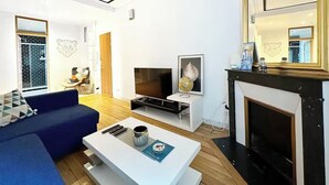 Een moderne woonkamer met een blauwe bank, een witte salontafel, een flatscreen televisie en een open haard.