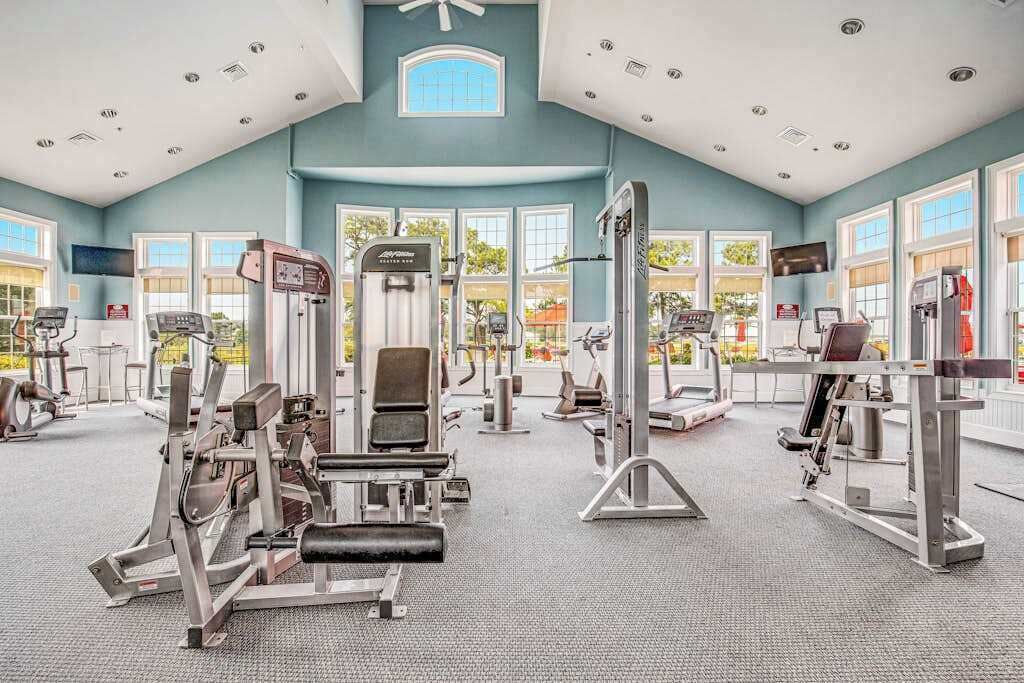 Ein Fitnessstudio mit verschiedenen Trainingsgeräten, großen Fenstern und hoher Decke.