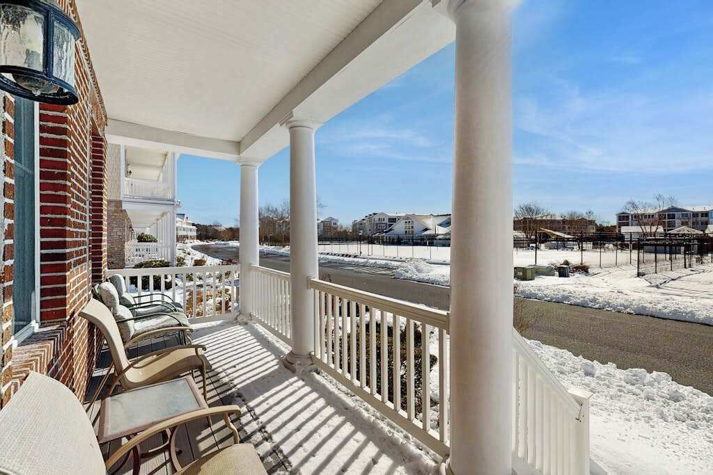 A covered porch with white railings, a brick wall, and outdoor furniture.