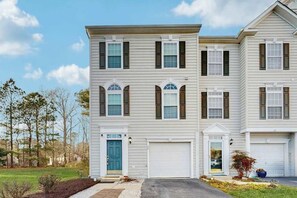 A two-story residential building with a front garage, a blue door, and a well-maintained lawn. - Townhomes of Providence dog-friendly townhouse w/shared pool, deck, W/D (Ocean View)