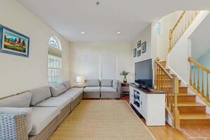 A living room with a sectional sofa, a TV, a staircase, and a large window. - Townhomes of Providence dog-friendly townhouse w/shared pool, deck, W/D (Ocean View)