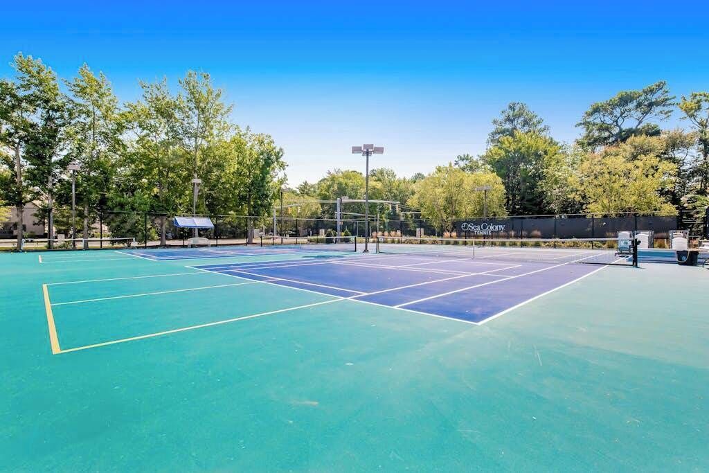A tennis court with a net, surrounded by trees and a fence.