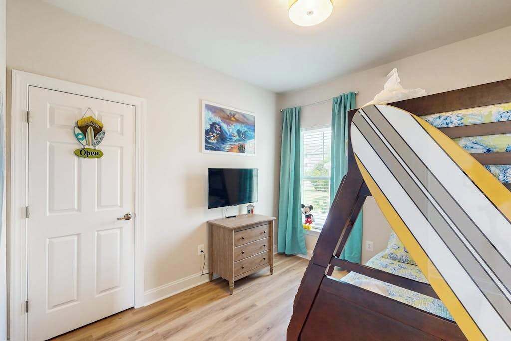 Una habitación con cama, televisión, cómoda y una puerta con un letrero.