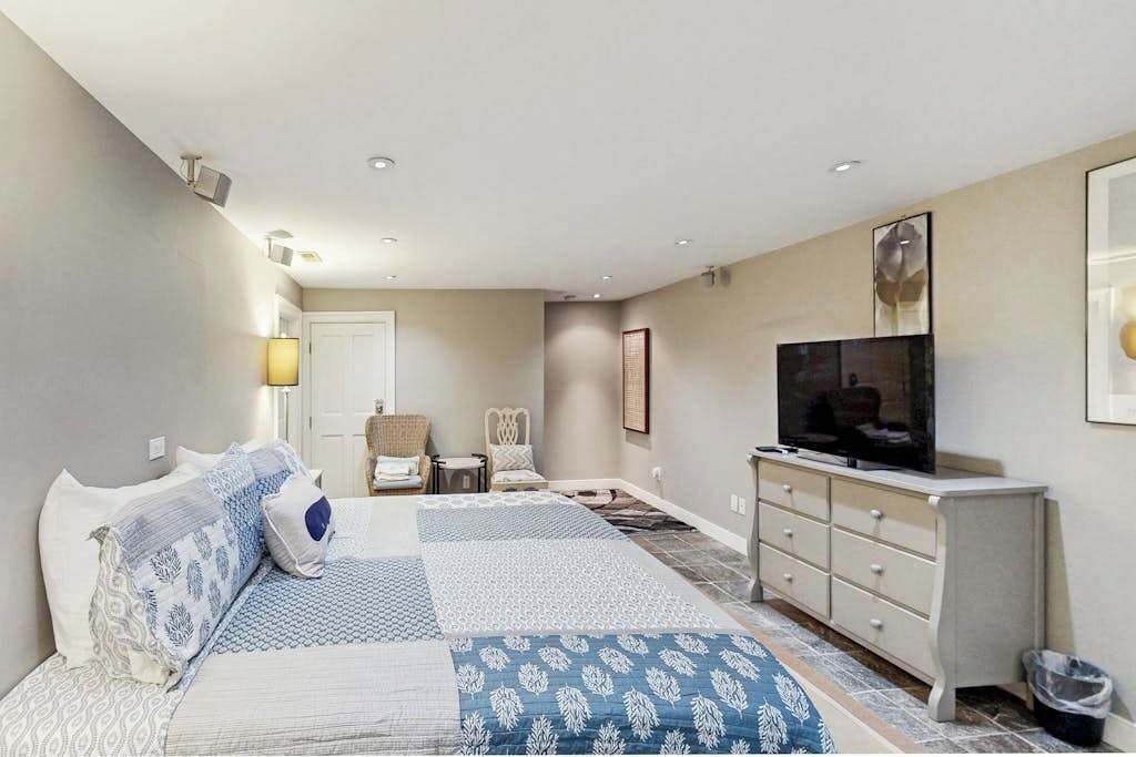 A bedroom with a bed, a TV, a dresser, a chair, and a small table.