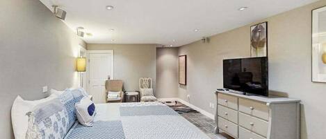 A bedroom with a bed, a TV, a dresser, a chair, and a small table.