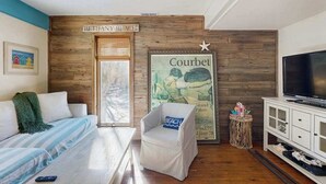 Ein Zimmer mit einer Holzwand, einem Fernseher, einem Sofa, einem Sessel, einem Poster und einem Schild mit der Aufschrift 'BETHANY BEACH'.