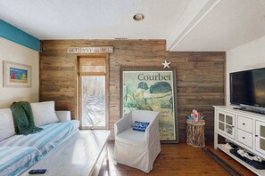 Ett rum med en väggpanel av trä, en tv, en soffa, en stol, en affisch och en skylt med texten ”BETHANY BEACH”.