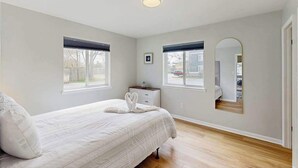 A bedroom with a bed, two windows, a nightstand, a mirror, and a door. - Henlopen Station condo w/shared pool, patio, grill, close to beach & restaurants (Rehoboth Beach)