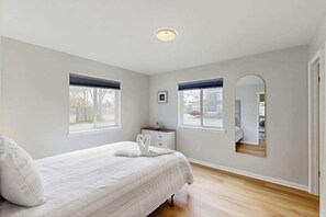 A bedroom with a bed, two windows, a nightstand, a mirror, and a door. - Henlopen Station condo w/shared pool, patio, grill, close to beach & restaurants (Rehoboth Beach)