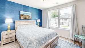 Un dormitorio con cama, dos mesitas de noche con lámparas, una ventana con vistas y una pared azul de acento.
