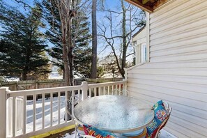 Ein überdachter Außenbereich mit einem Metalltisch und -stühlen, einem weißen Geländer und Schnee auf dem Boden.
