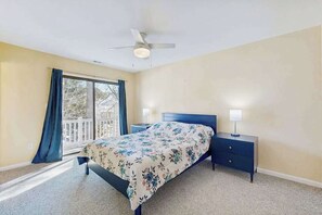Ein Schlafzimmer mit einem Bett, Nachttischen, einem Deckenventilator und einem Fenster mit Vorhängen.
