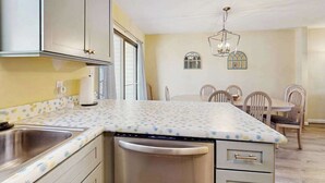A compact kitchen with a dishwasher, a sink, and a dining area with chairs and a table. - Bethany Pines townhouse w/community pool & tennis, close to beach (Bethany Beach)