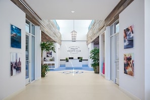 A modern lobby with a reception desk, a sign reading 'Welcome to the Health Aquatic Club,' and glass doors leading to other areas.