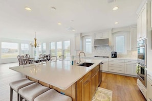 A spacious kitchen with a large island, white cabinetry, and a view through the windows.