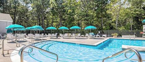 Une piscine entourée d’arbres, avec des chaises longues et des parasols.