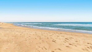 Een strand met voetafdrukken in het zand en een helderblauwe lucht.