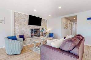 Ein Wohnzimmer mit Backsteinwand, Flachbildfernseher, Kamin, Sofa, Sessel und Couchtisch.