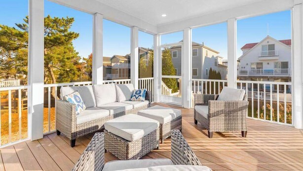 A covered outdoor deck with wicker furniture and a view of surrounding houses. - Town of Bethany Beach home with a fireplace & outdoor living - near beach (Bethany Beach)