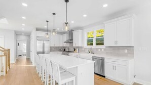 A modern kitchen with white cabinetry, a central island with bar stools, and pendant lighting. - Town of Bethany Beach home with a fireplace & outdoor living - near beach (Bethany Beach)