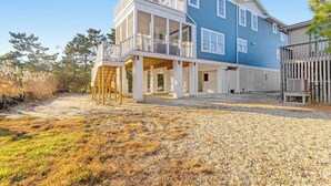 A two-story house with a balcony, a covered porch, and a gravel driveway. - Town of Bethany Beach home with a fireplace & outdoor living - near beach (Bethany Beach)