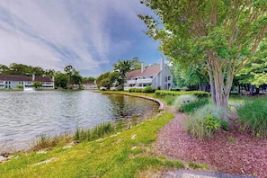 A lakeside property with a house, a pond, and surrounding greenery. - Sea Colony - 33577 West Lake View, Unit 1006B | Condo in Bethany Beach (Bethany Beach)